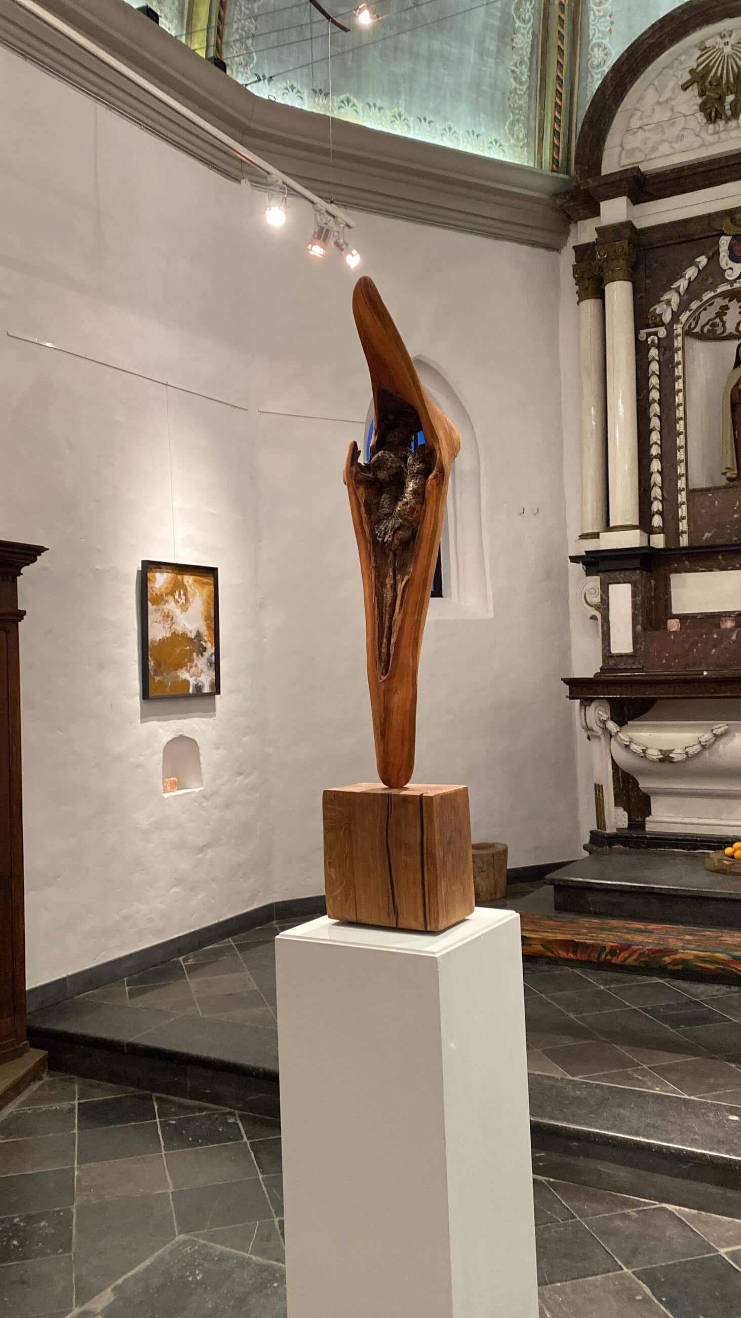 Een gesneden houten beeld op een sokkel in het kerkje, met de gewelven erachter.