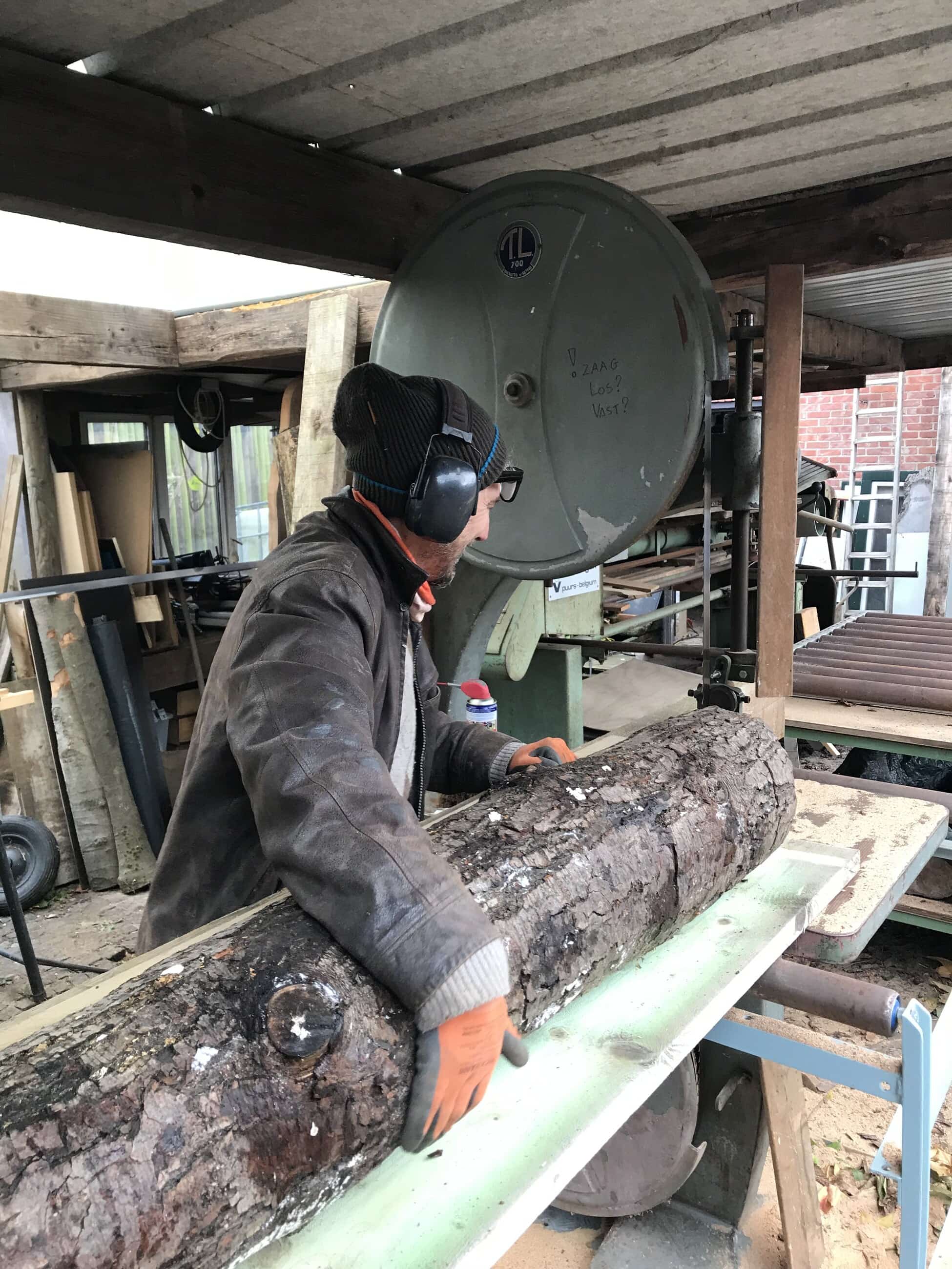 Bert Lemmens legt een ruwe stam op de rollenbaan van zijn lintzaag.