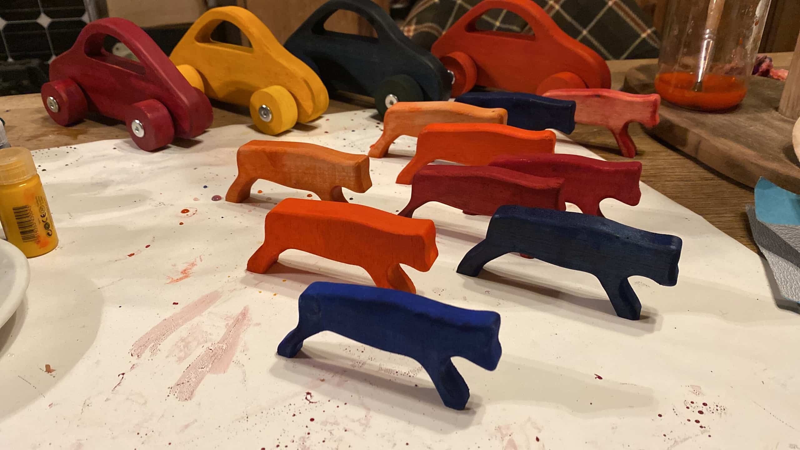 Houten speelgoed op een werkbank: autootjes en dierfiguren, deels geschilderd in rood, oker en donkerblauw.