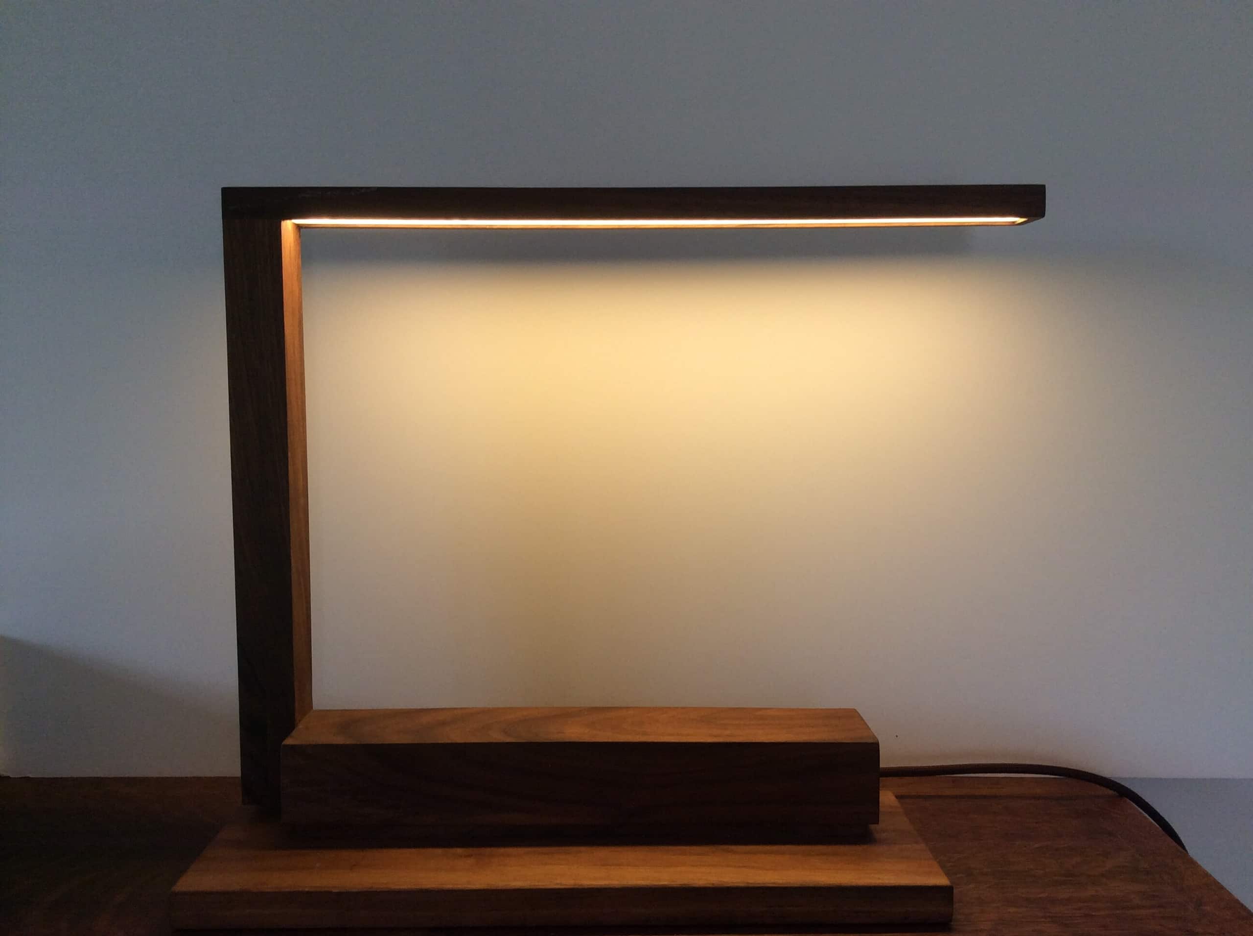 Een lamp uit hout, waarvan de arm het licht als een dunne lijn laat vallen.
