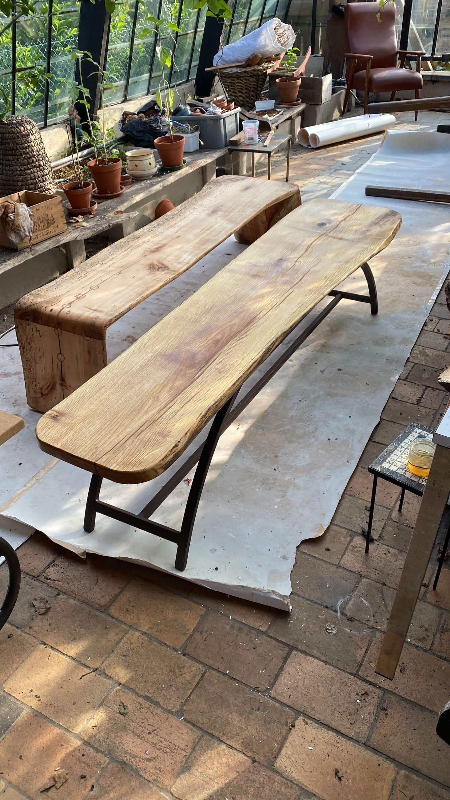 Een lange bank uit één plank met onbewerkte rand, rustend op een smal stalen onderstel.