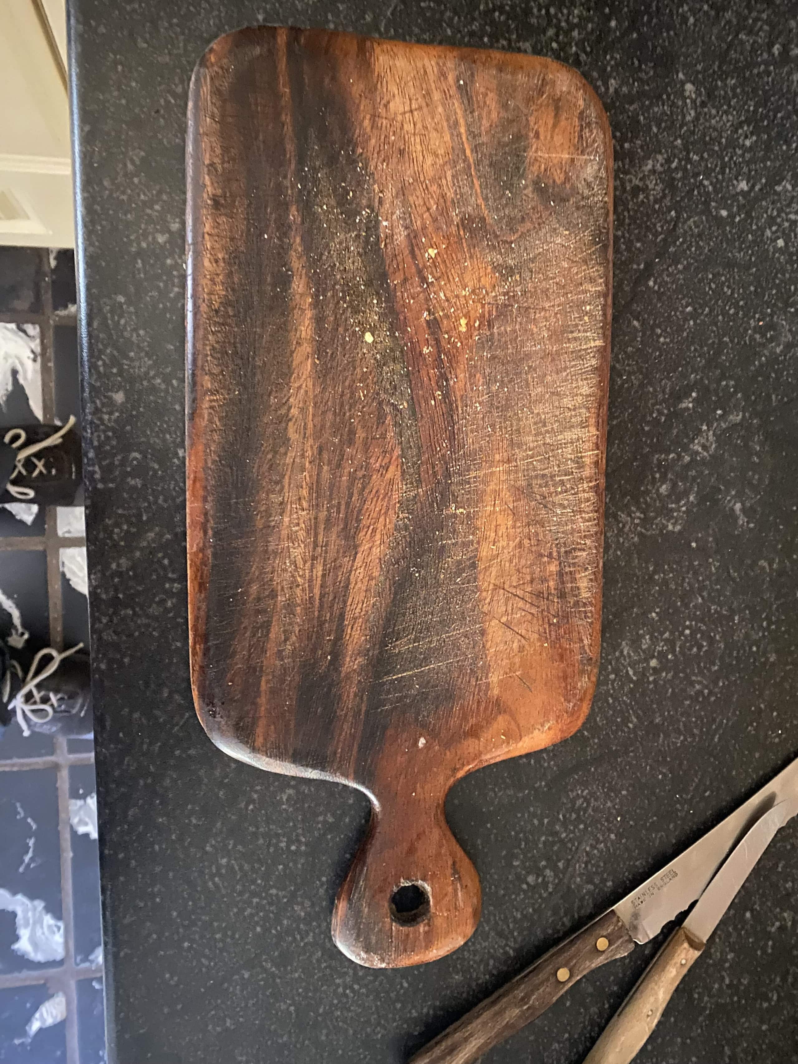 Een donkere notelaren plank met handgreep op een stenen blad, naast een mes.